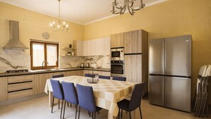 Une cuisine moderne avec une table à manger, des chaises, un lustre et des appareils électroménagers en acier inoxydable.