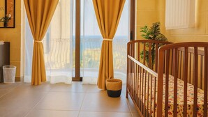 Une chambre avec un berceau, une fenêtre avec des rideaux, une plante et une vue sur l’extérieur.