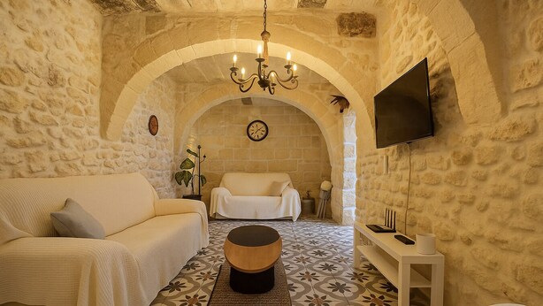 Une pièce chaleureuse aux murs de pierre, avec un canapé, un fauteuil, une petite table et un téléviseur fixé au mur.