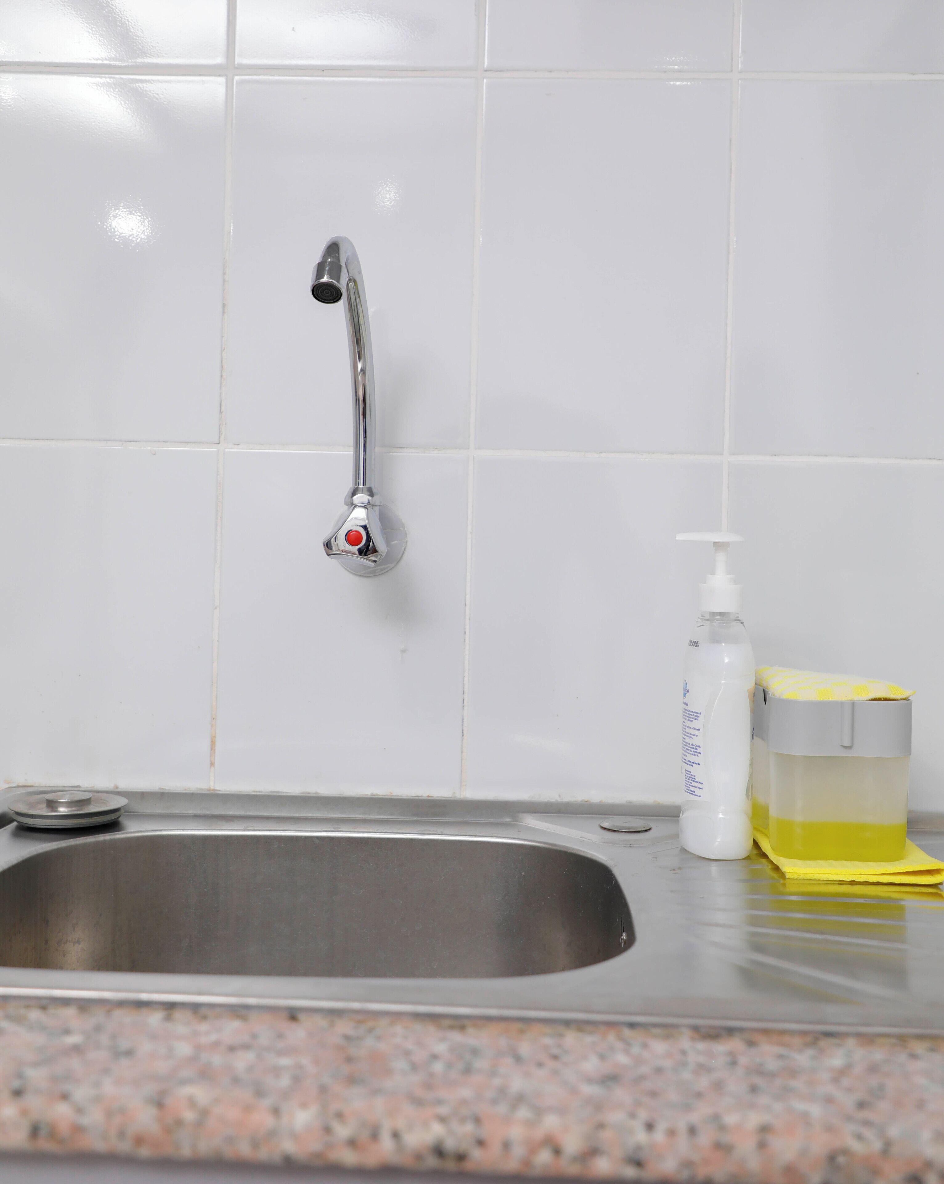 A stainless steel kitchen sink with a faucet, a soap dispenser, and a yellow sponge on a granite countertop.
