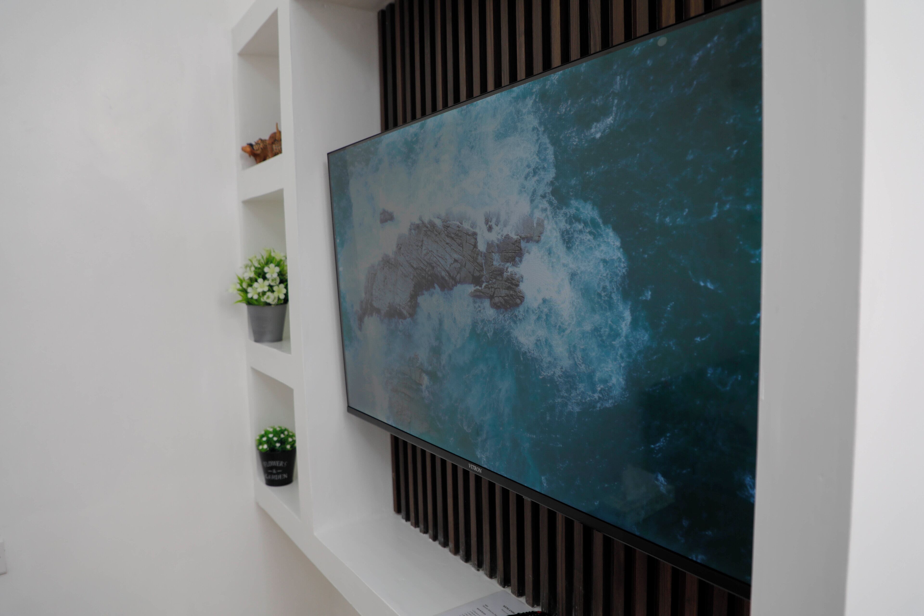 A flat-screen TV mounted on a white wall with a wooden panel design.
