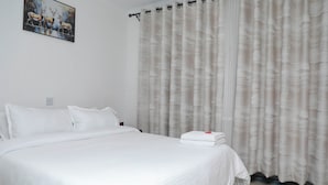 A hotel room with a large bed, white bedding, a painting on the wall, and a curtain with a wavy pattern. - Nakuru Guest Suites (Nakuru)
