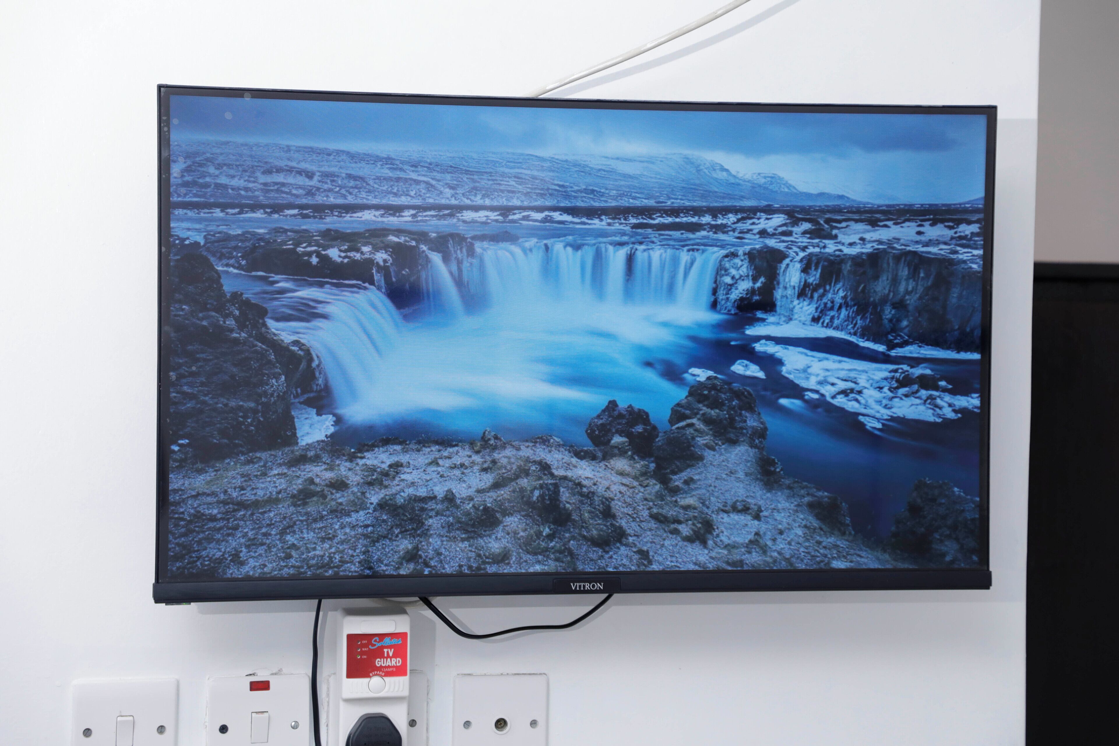 A flat-screen TV mounted on a wall displaying a waterfall scene.