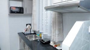 A compact kitchenette with a microwave, sink, and stainless steel cabinets. - Nakuru Guest Suites (Nakuru)