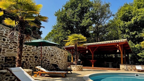 Ein Poolbereich mit Liegestühlen, einer Steinmauer, einer Holzpergola und einem Pool.
