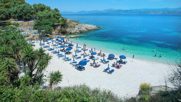 A beach with white sand, clear blue water, and numerous blue umbrellas. - Orizzonte Blu - Three Bedroom Villa, Sleeps 6 (Corfu)