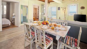 A dining area with a table set for breakfast, a sofa, and a TV. - Orizzonte Blu - Three Bedroom Villa, Sleeps 6 (Corfu)