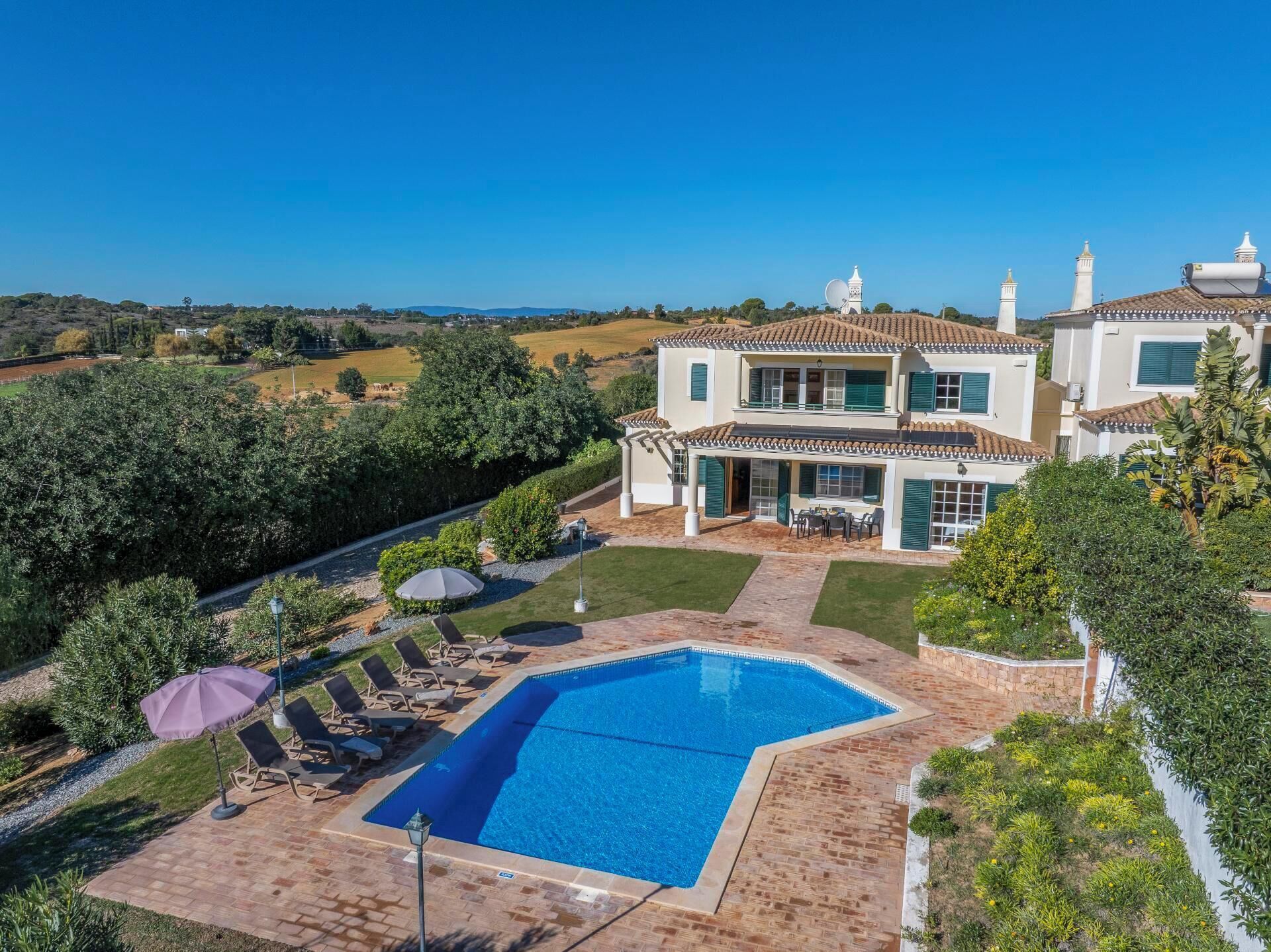 A two-story house with a swimming pool, outdoor seating, and a view of the countryside.