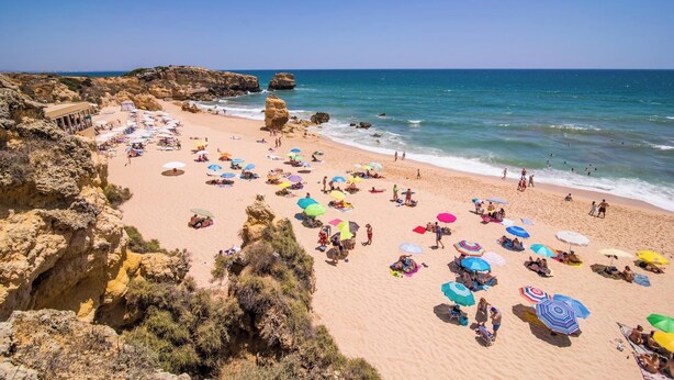 Una playa con muchos sombrillas de colores y gente disfrutando de la arena y el mar.