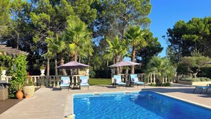 Piscina com espreguiçadeiras e guarda-sóis, cercada por árvores e um balaustrada de pedra.
