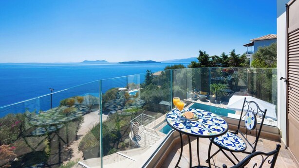 Un balcón con barandilla de cristal que ofrece vistas panorámicas del mar y montañas lejanas.
