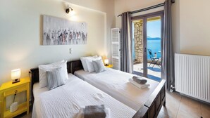 Un dormitorio con dos camas, un cuadro en la pared, vista al mar a través de un ventanal de vidrio y techo de madera.