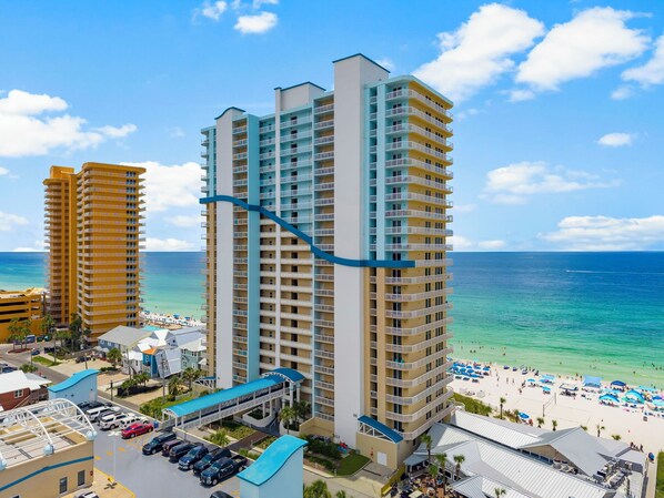 A high-rise hotel with multiple balconies, a beach view, and a parking area.
