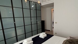 Una habitación de hotel moderna con una cama grande, un corredor de cama azul oscuro y una pared divisoria de vidrio.