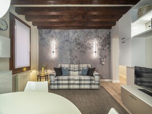 Une chambre moderne avec un canapé à carreaux, un téléviseur et un mur décoratif orné de motifs de feuilles.