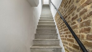 Una escalera de piedra con peldaños que conducen a una plataforma, flanqueada por paredes blancas y una pared de ladrillo.