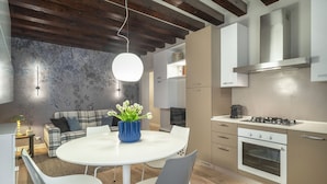 Una cocina moderna con armarios blancos, una mesa redonda con sillas y un jarrón azul con flores.