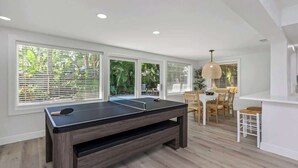 A pool table in a room with large windows, a dining area, and a hanging light fixture. - Resort Backyard! Heated Pool! Pool Table! PingPong (Largo)