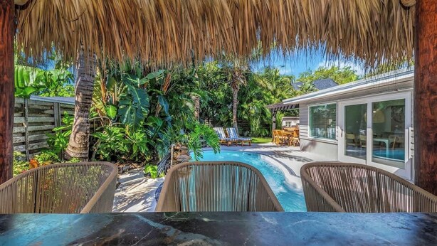 A pool area with a thatched roof, lounge chairs, and a house with large windows. - Resort Backyard! Heated Pool! Pool Table! PingPong (Largo)