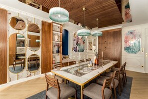 A spacious dining area with a marble table, wooden chairs, and pendant lighting. - Merveil Luxury Suite - Louvre Michodiere (Paris)