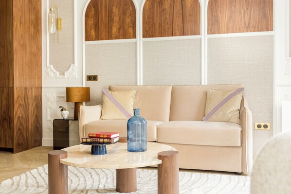 A living room with a beige sofa, a round coffee table, and a lamp. - Merveil Luxury Suite - Louvre Michodiere (Paris)