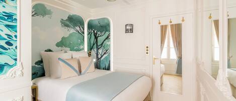 A bedroom with a bed, a ceiling fan, a door with a mirror, and a wall with a tree mural.