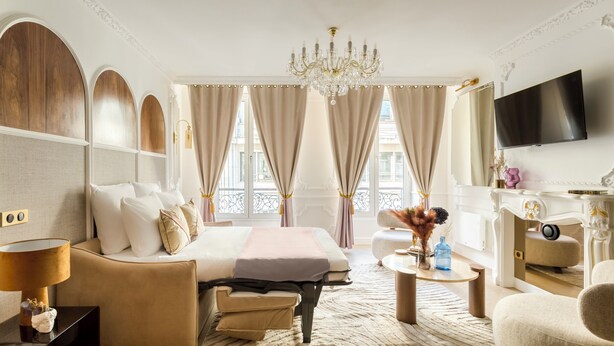 Et rummeligt hotelværelse med en stor seng, et siddeområde med sofa og lænestol, et skrivebord med stol og et fjernsyn ophængt på væggen.