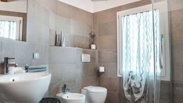 A modern bathroom with a large sink, bidet, and glass shower enclosure.