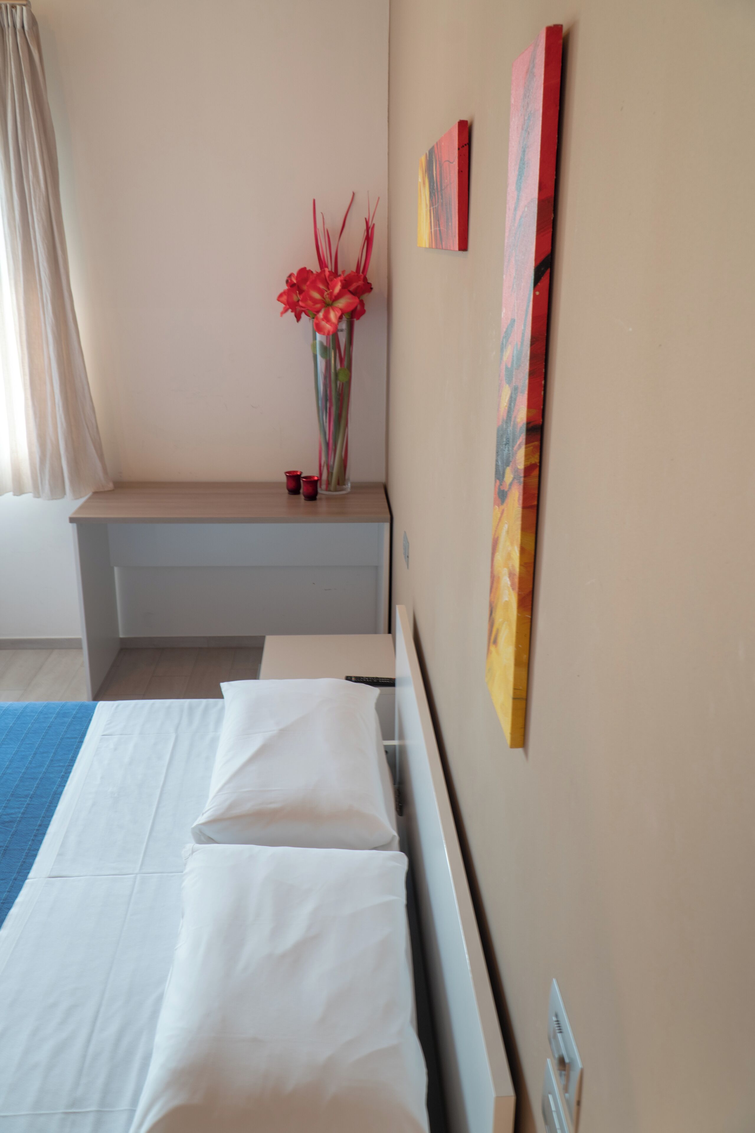 Ein Hotelzimmer mit einem Bett, einem Schreibtisch, einer Blumenvase und zwei Bildern an der Wand.