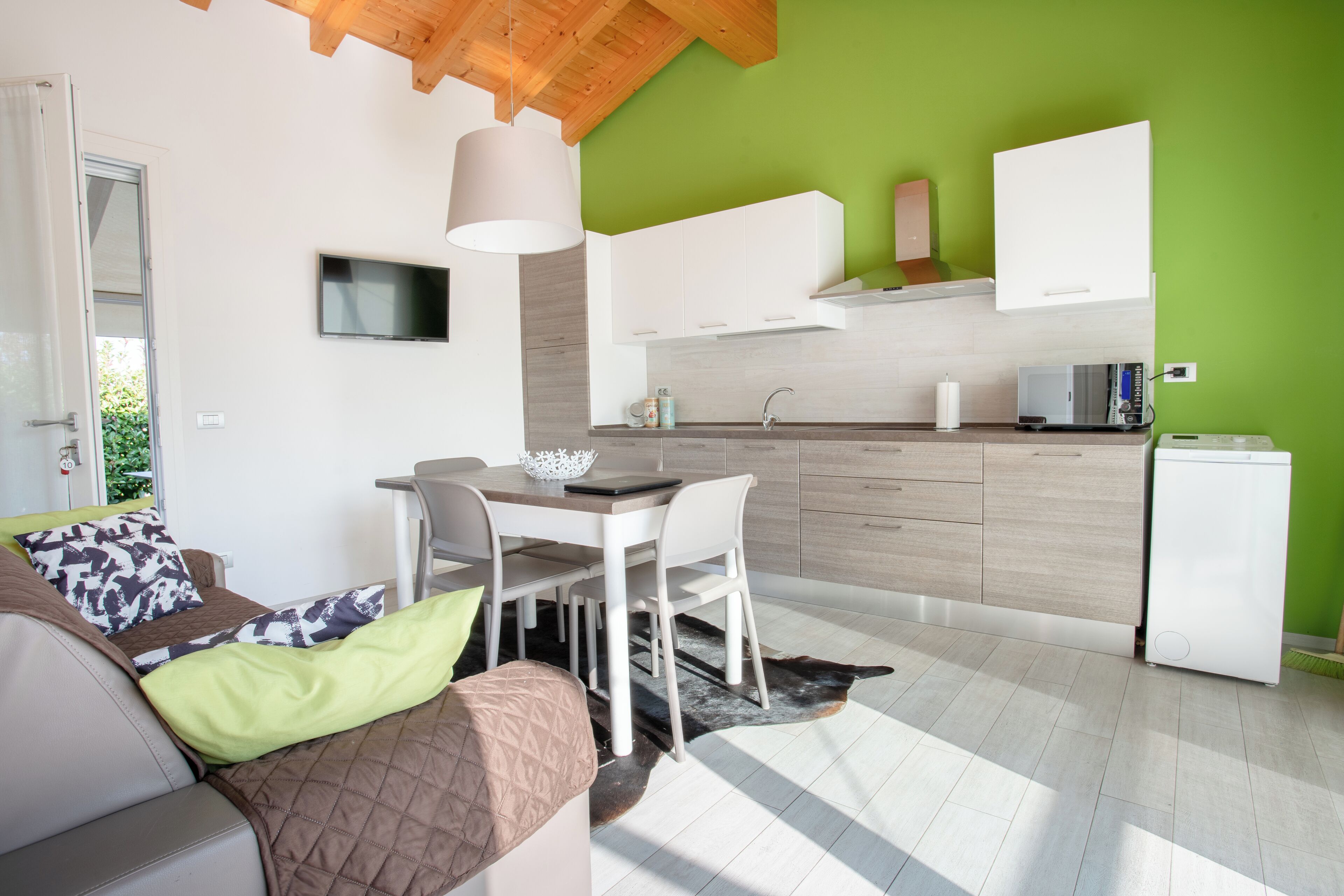 A modern living room with a sofa, a dining table, and a kitchen area with white cabinets and a green wall.