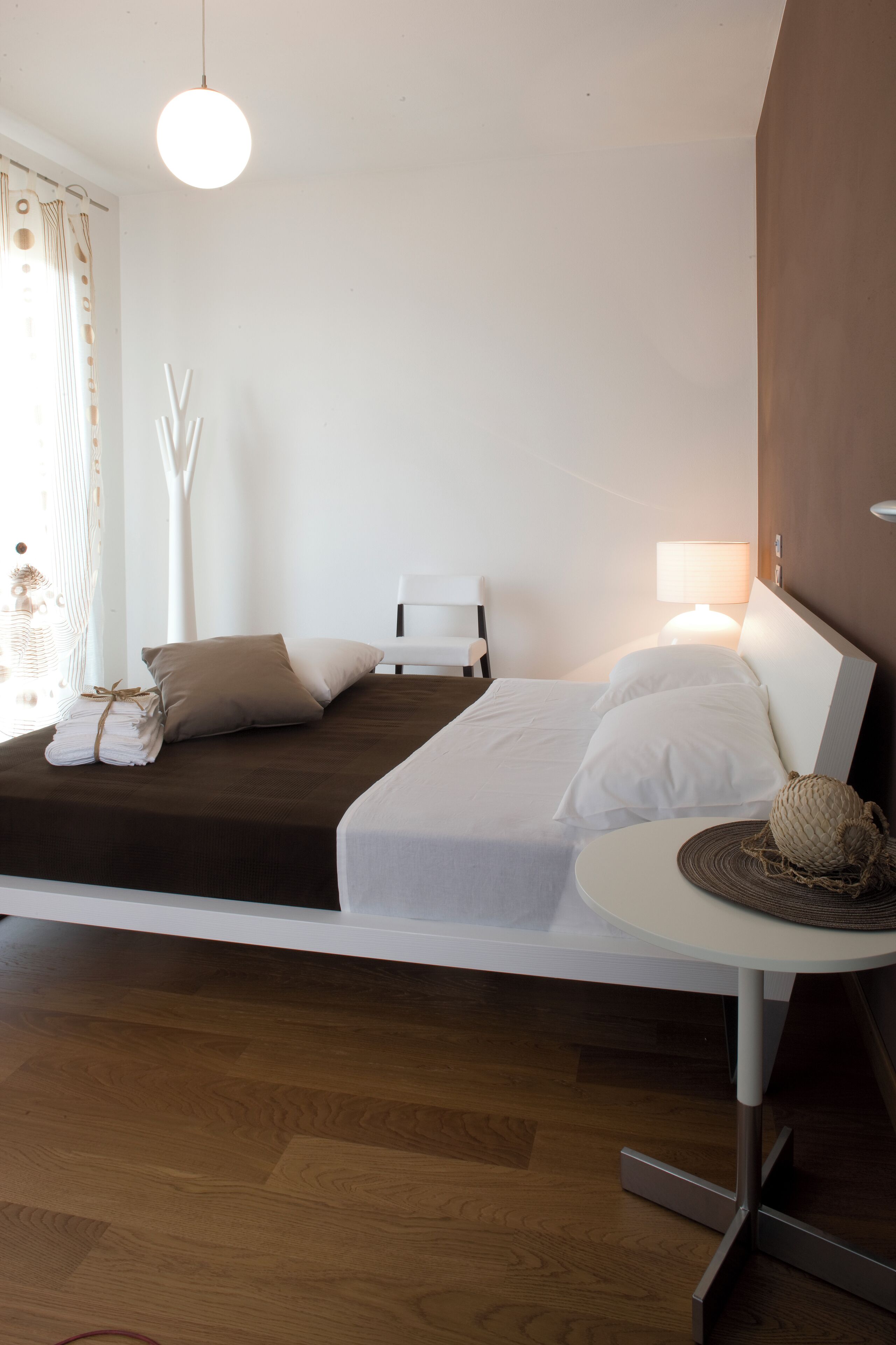 A modern hotel room with a bed, bedside table, lamp, and a view of the outside.