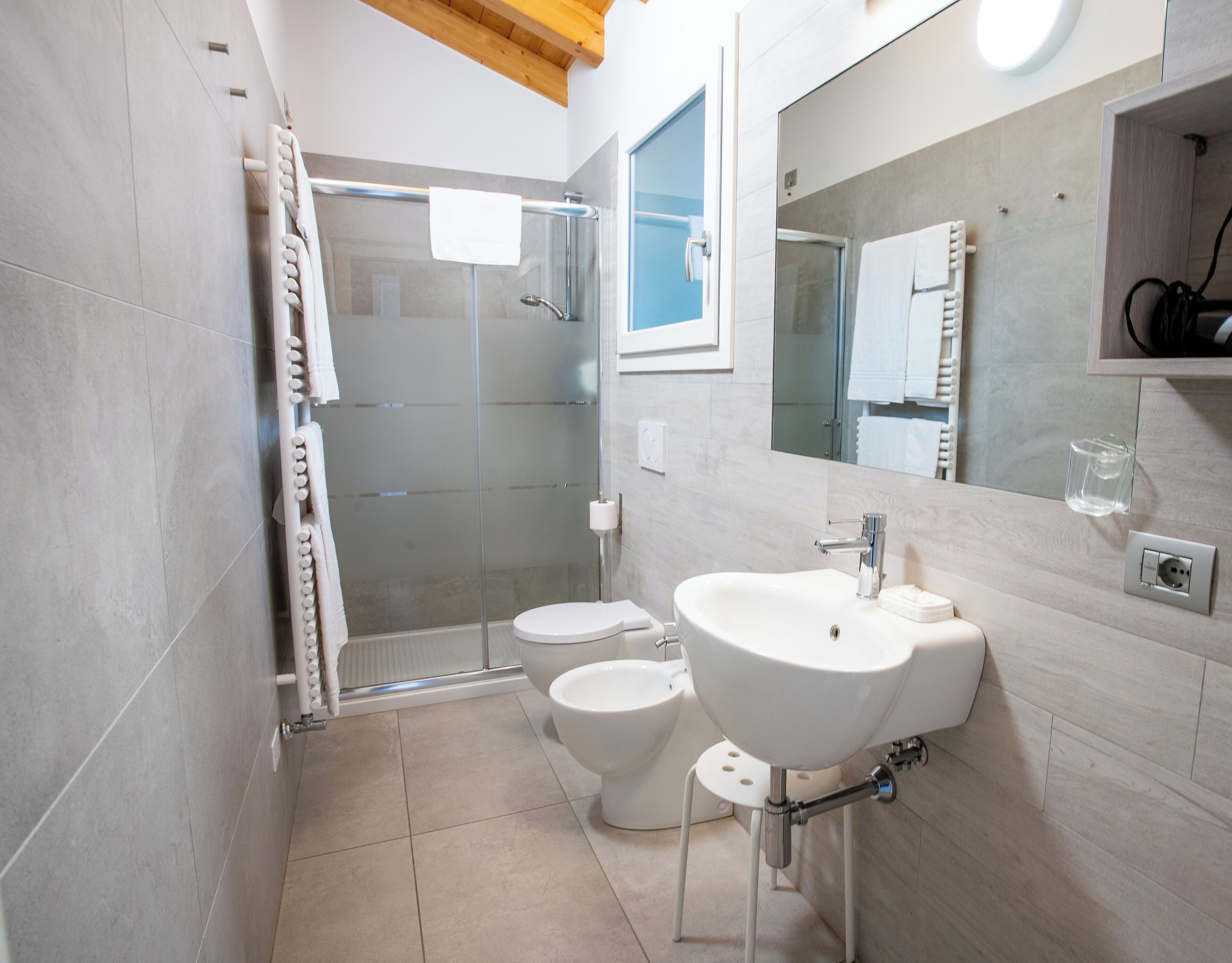 A modern bathroom with a glass-enclosed shower, two toilets, a sink, and a mirror.