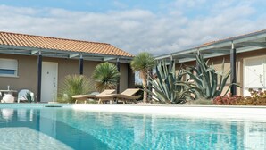 A swimming pool with lounge chairs and palm trees, surrounded by buildings with a tiled roof. - Magrine Castelfranco Veneto  (Castelfranco Veneto)