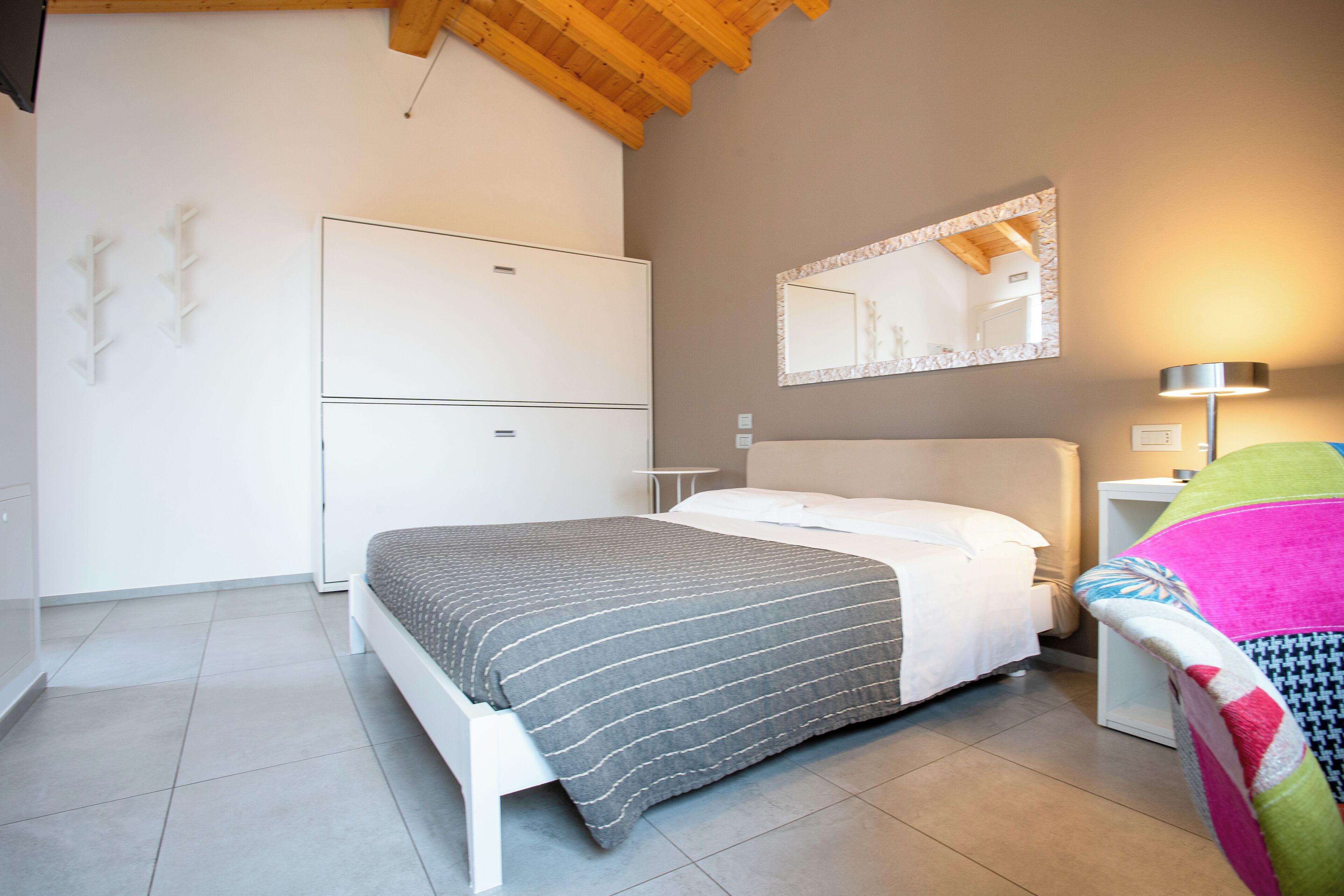 Quarto com cama, guarda-roupa, espelho e mesa de cabeceira com abajur.