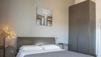 A modern bedroom with a wooden ceiling, a bed with a grey striped bedspread, a grey wardrobe, and a wall-mounted abstract painting.