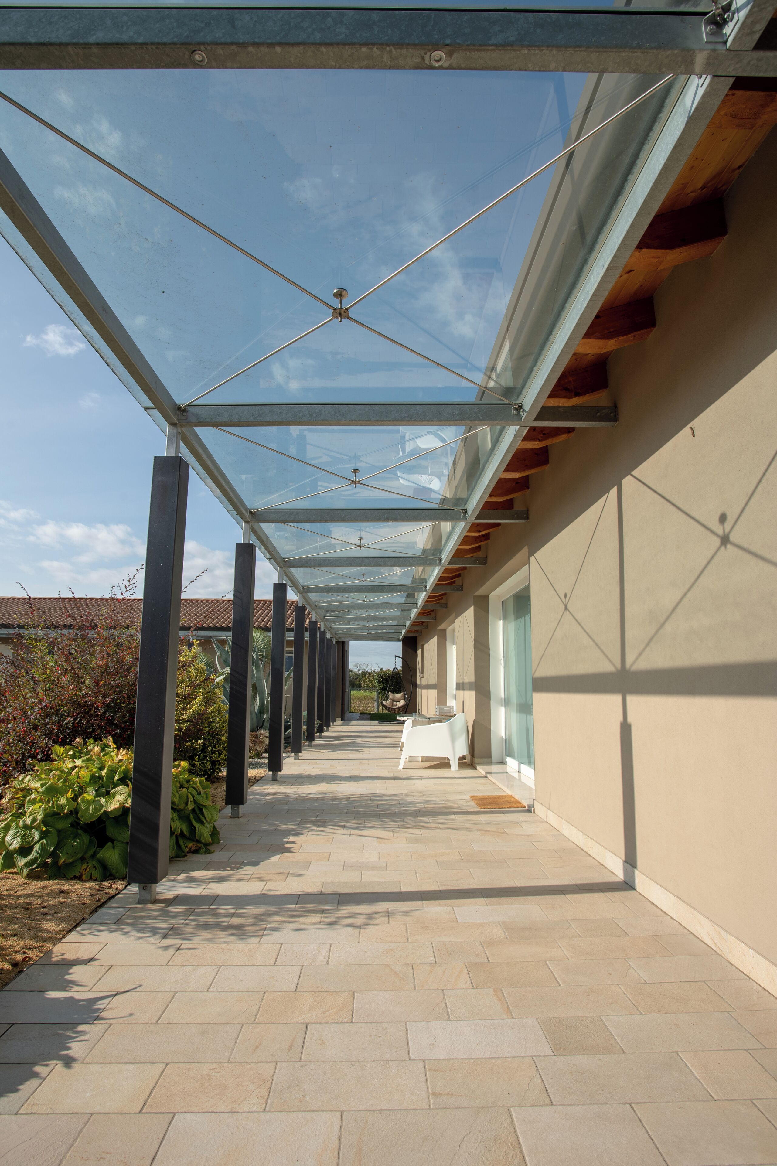 A covered outdoor corridor with a glass roof, a tiled floor, and a view of a building in the background.