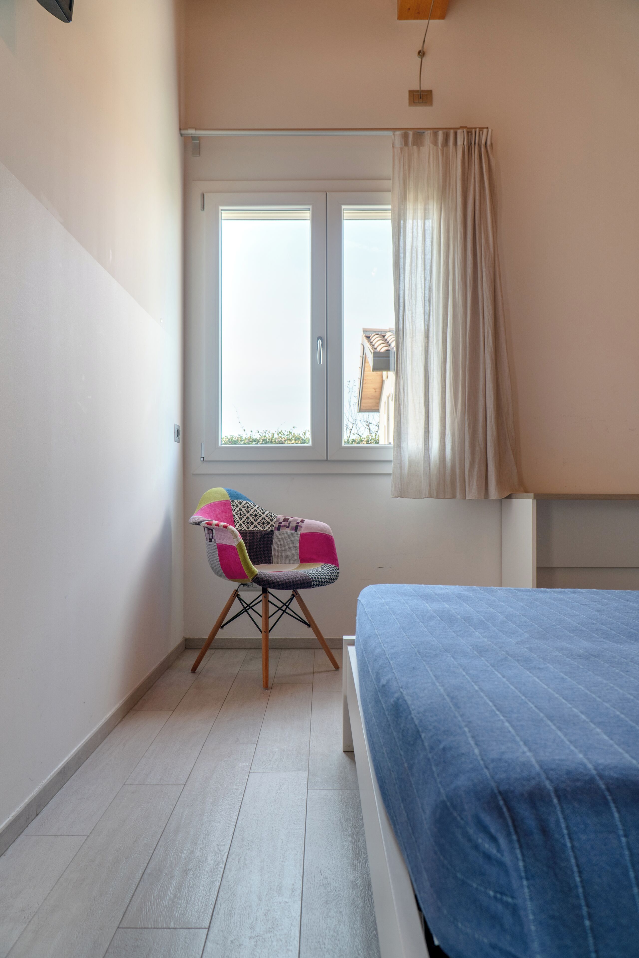 A bedroom with a bed, a window with curtains, and a colorful chair.