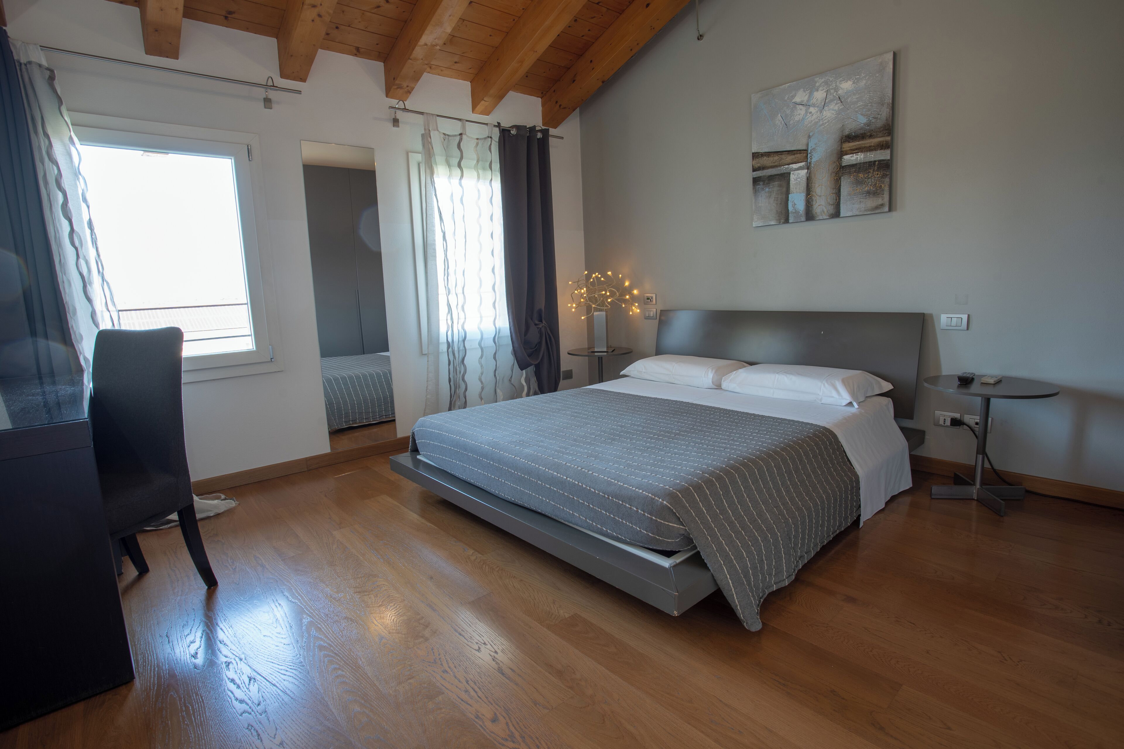 Un dormitorio con cama, una silla, una mesita y una ventana.