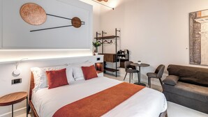 Una habitación de hotel moderna con una cama grande, un área de descanso con un sofá y sillas, una mesita y un perchero en la pared.