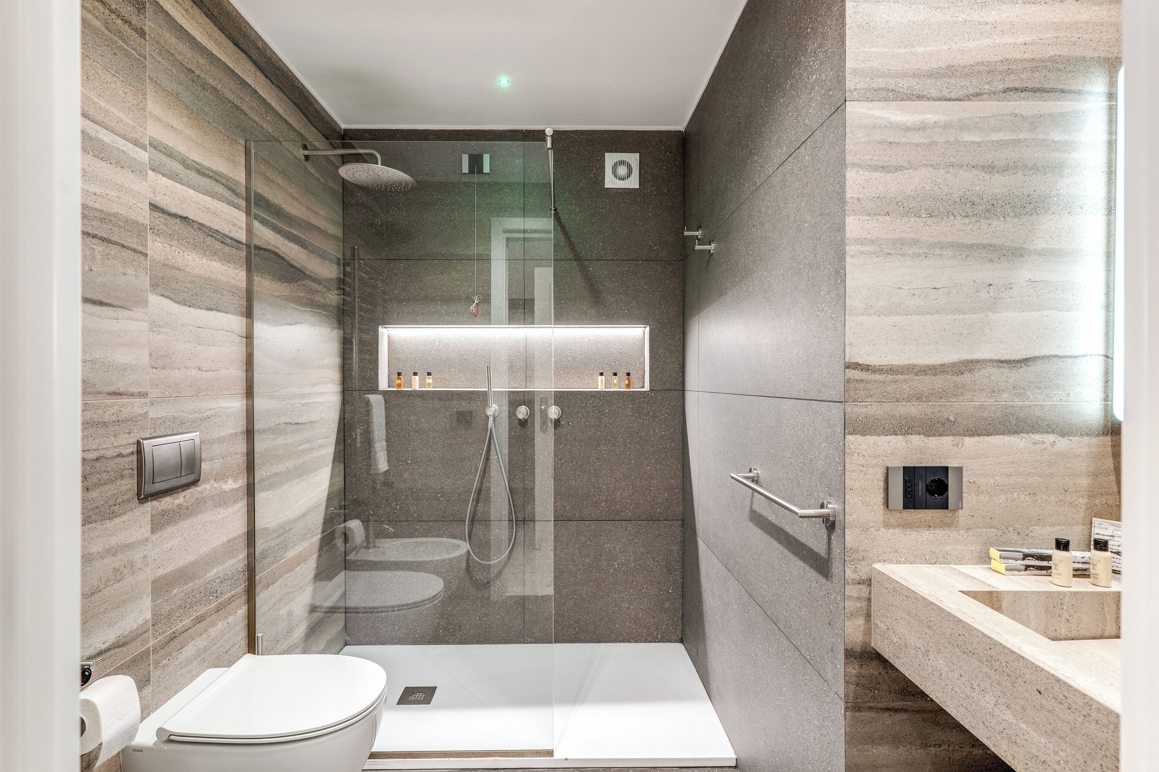 Et moderne badeværelse med en glasafskærmet brusekabine, toilet og en vaskebord med håndvask.