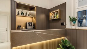 Una zona de bar moderna con encimera de mármol, estanterías con botellas, una máquina de café y una planta en maceta.