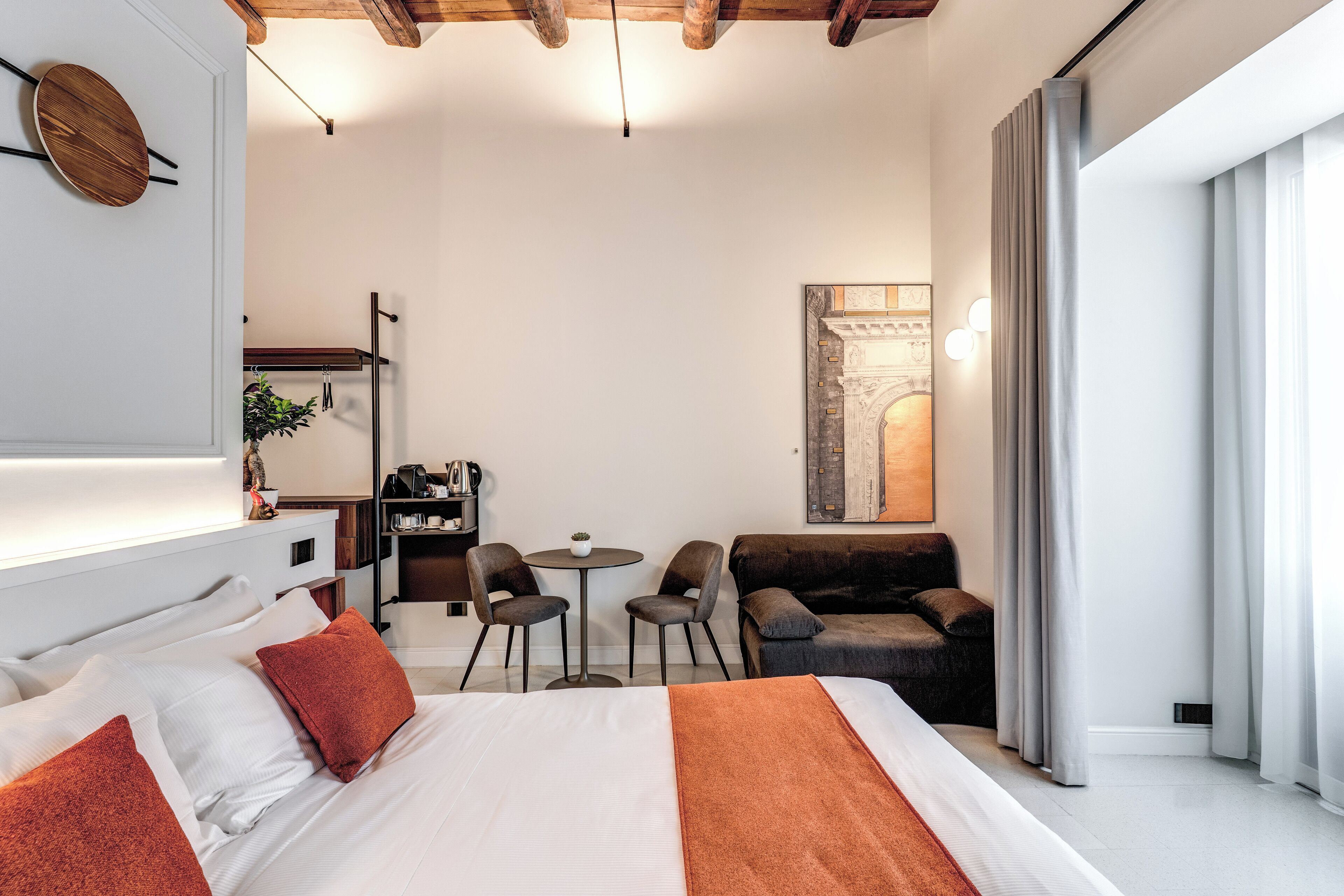Ein modernes Hotelzimmer mit einem großen Bett, einem Schreibtisch, zwei Stühlen, einer Couch und Blick auf eine Stadtlandschaft durch das Fenster.