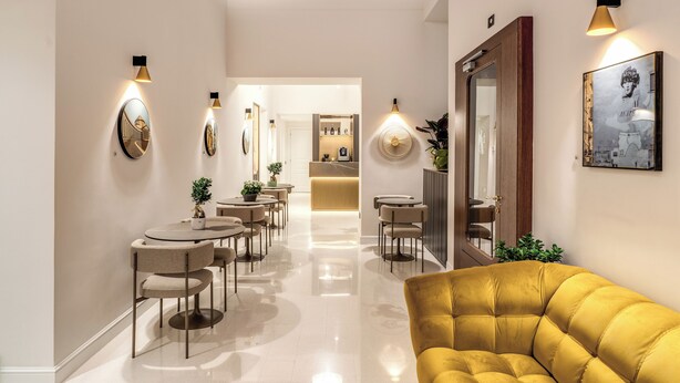 Un interior moderno con un pasillo central, mesas redondas y un sofá amarillo.