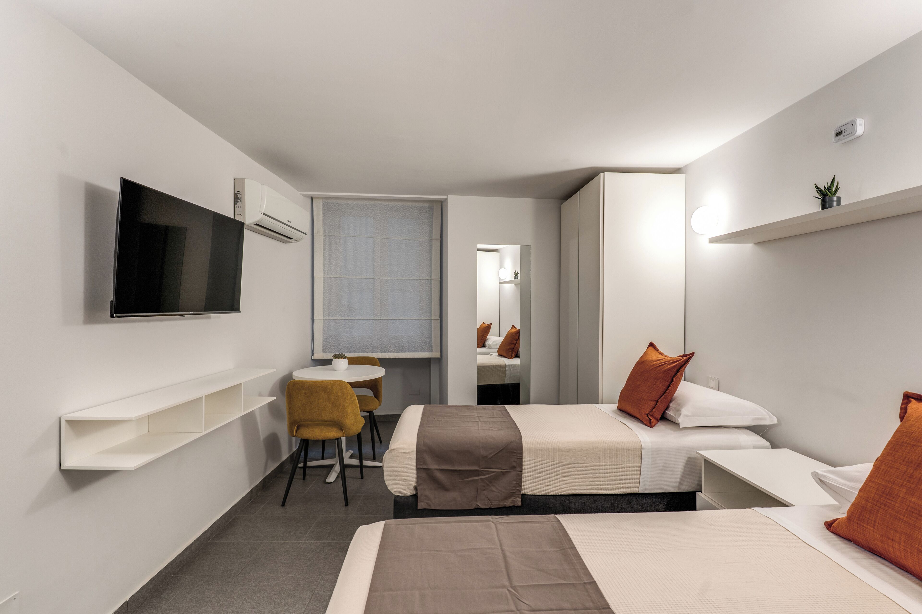 Une chambre d’hôtel avec un lit, un bureau, une chaise, un téléviseur fixé au mur et une petite étagère.