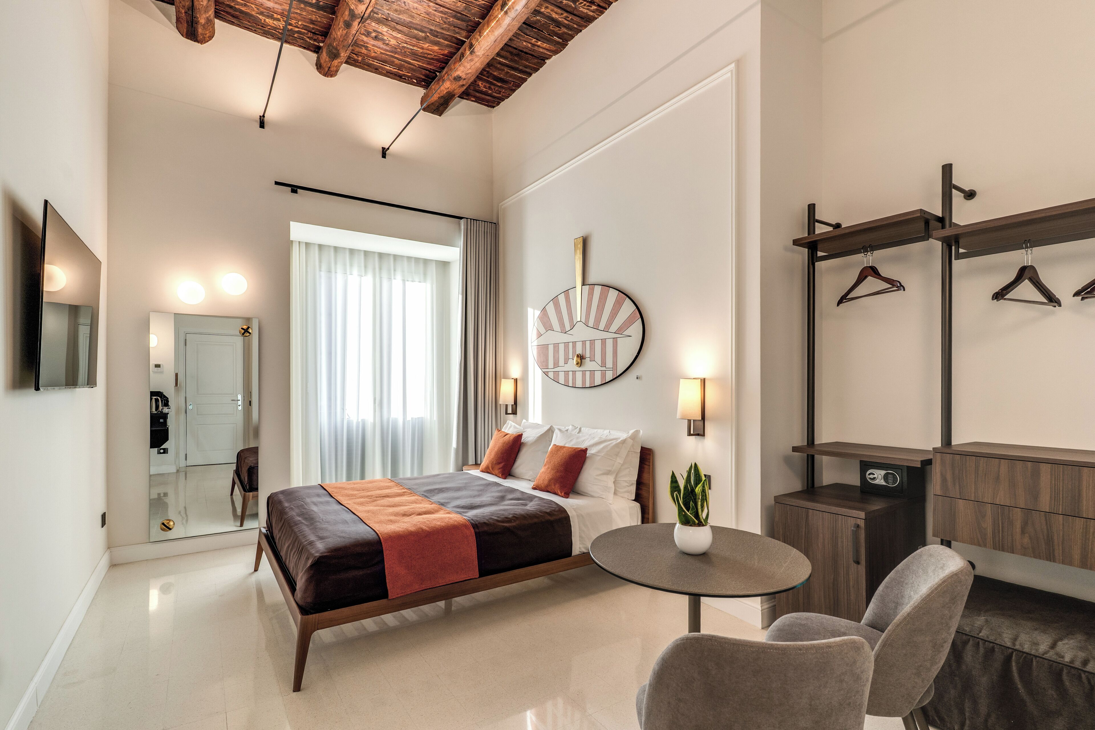 A modern hotel room with a bed, bedside table, chair, and a mirror.