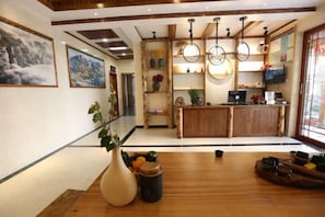 Een hotellobby met een houten receptiebalie, een grote vaas met planten en kunstwerken aan de muren.
