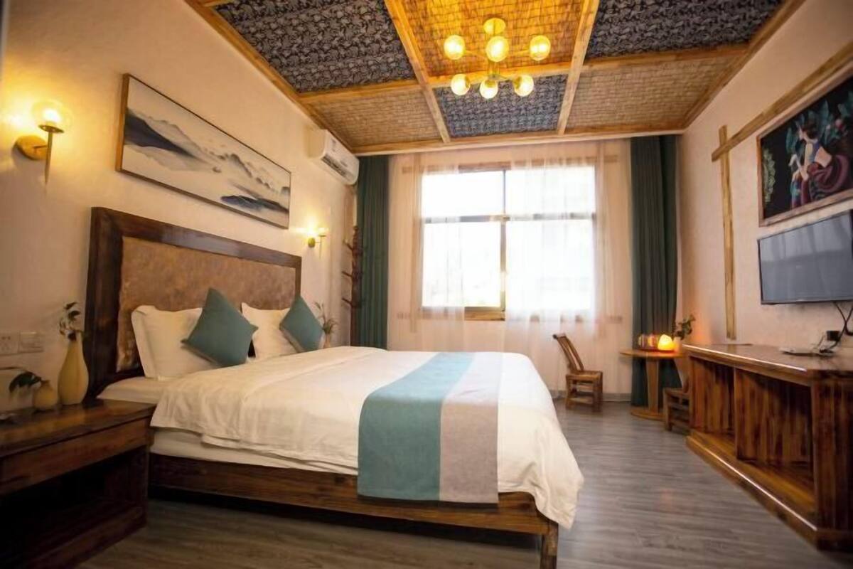 Een slaapkamer met een bed, houten hoofdbord, nachtkastjes, een bureau, een stoel, een televisie en een raam met gordijnen.