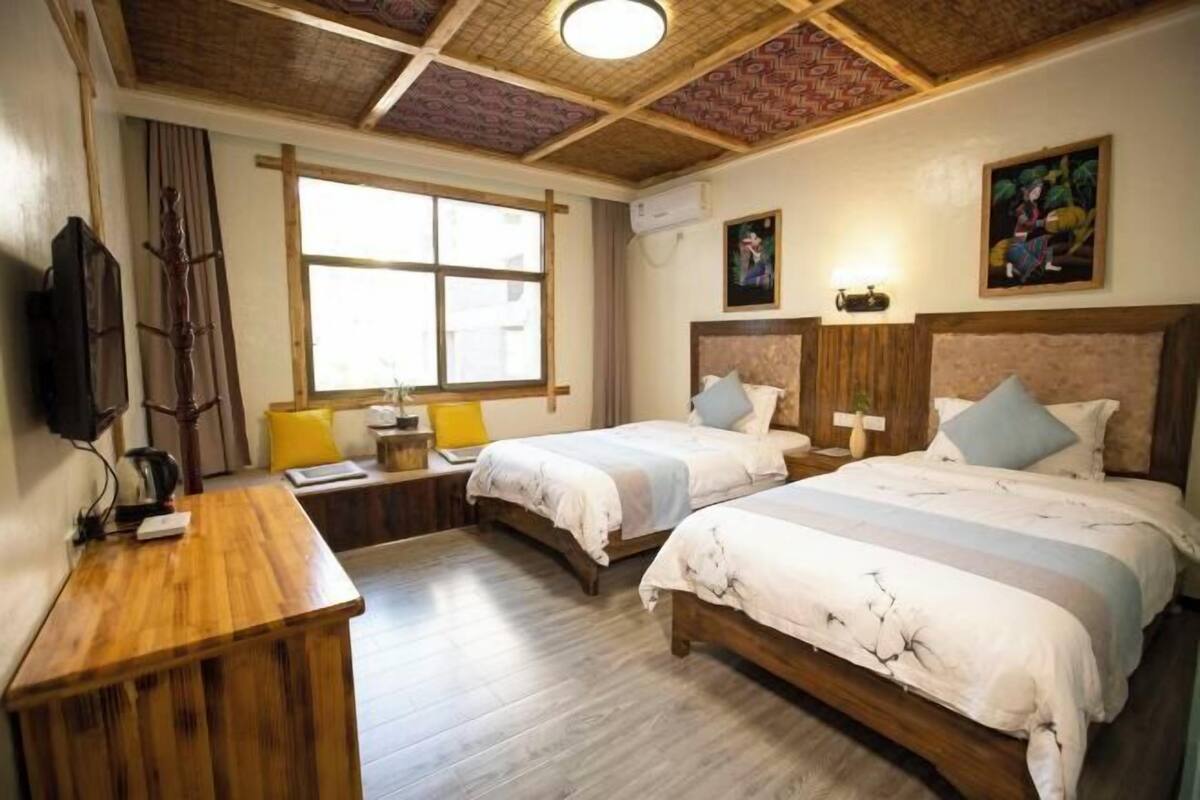Een hotelkamer met twee bedden, een houten bureau, een raam en een plafond met houtstructuur.