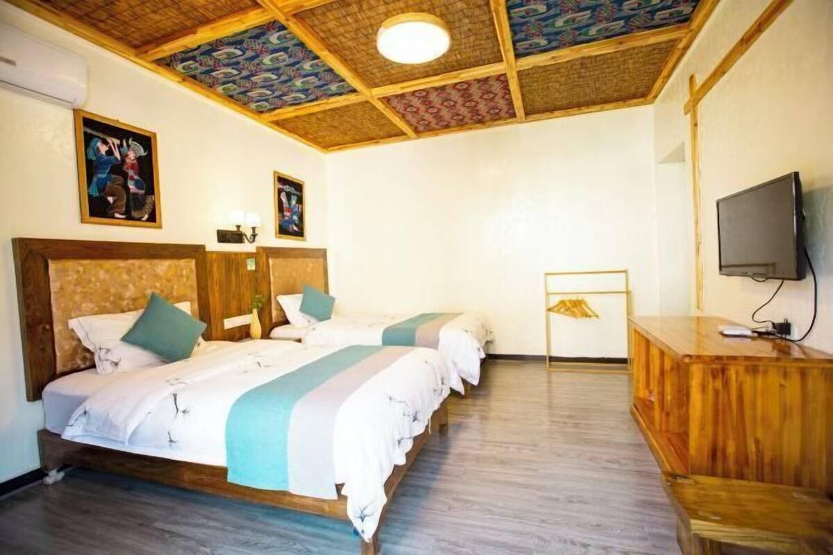 Een hotelkamer met twee bedden, een houten hoofdbord, een televisietoestel en een plafond met een gedessineerd patroon.