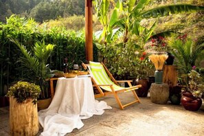Eine Terrasse mit einem Holzstuhl, einem Tisch mit weißem Tuch und verschiedenen Kübelpflanzen.